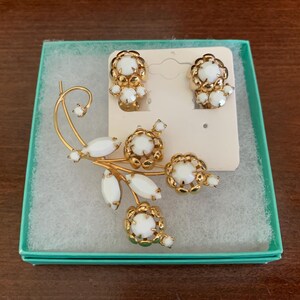 May include: A vintage jewelry set featuring a gold-tone brooch and matching clip-on earrings. The brooch has a floral design with white cabochon stones and gold accents. The earrings also have a floral design with white stones.