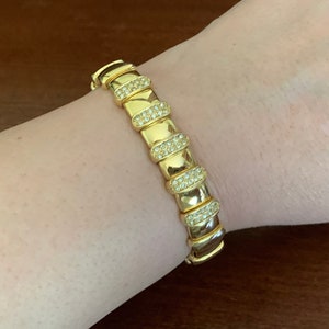 May include: A gold bracelet with a row of oval-shaped links, each set with clear rhinestones.