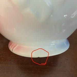 May include: A white ceramic vase with a pink and blue ombre glaze. The vase has a round body and a flared lip. The base of the vase has a small chip.