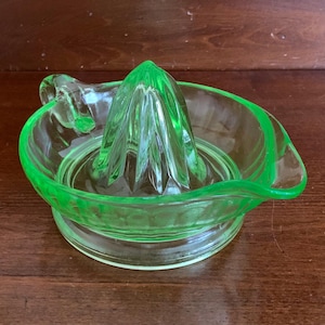 May include: A vintage, green glass citrus juicer. The juicer features a reamer and a bowl with a handle and a pouring spout. The glass has a vibrant, neon green hue, and the design is likely from the Art Deco era.