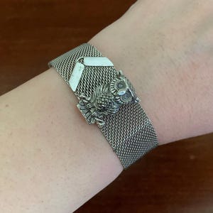 May include: A silver mesh bracelet with an owl charm. The owl is facing forward with its wings spread out.