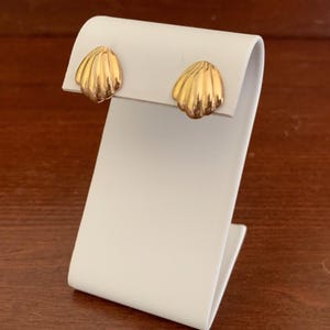 May include: A pair of gold-tone shell-shaped earrings on a white display stand.