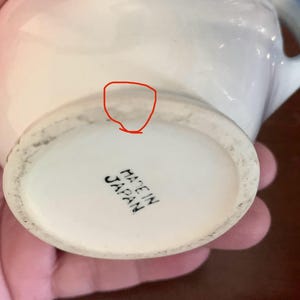 May include: White ceramic teacup with a blue and pink floral design. The bottom of the cup reads "Made in Japan".