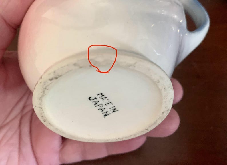 May include: White ceramic teacup with a blue and pink floral design. The bottom of the cup reads "Made in Japan".