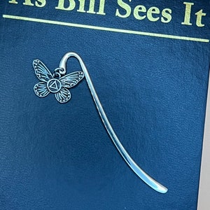 May include: Silver bookmark with a butterfly design. The butterfly has a silver body and wings with a black and white pattern. The bookmark is shaped like a long, thin rectangle with a curved top.