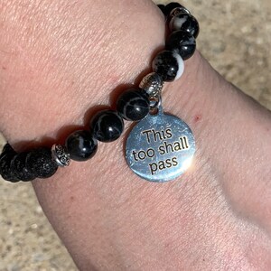 May include: Black and white beaded bracelet with a silver charm that reads "This too shall pass".