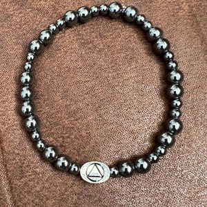 May include: A black beaded bracelet with a silver charm featuring a triangle symbol.