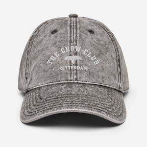 May include: A gray vintage-style baseball cap with the text "THE CROW CLUB" and "KETTERDAM" embroidered in white.