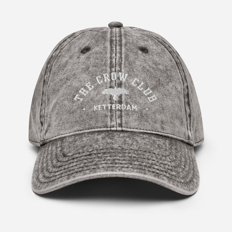 May include: A gray vintage-style baseball cap with the text "THE CROW CLUB" and "KETTERDAM" embroidered in white.