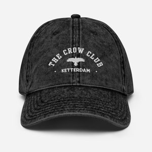 May include: A black vintage washed cotton baseball cap with white embroidery that reads "The Crow Club. Ketterdam."