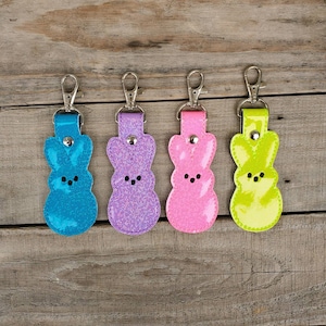 May include: Four colourful keychains shaped like Easter Peeps, each with a different colour: blue, purple, pink, and yellow.