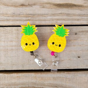 May include: Two yellow pineapple-shaped badge holders with smiling faces and green tops. The badge holders are attached to retractable badge reels.