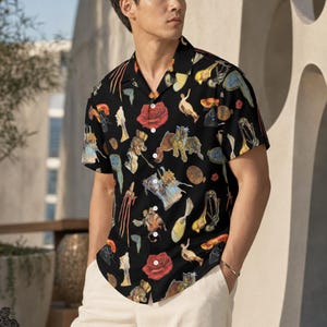 May include: A short-sleeved button-down shirt in black featuring a colourful, repeating artistic print of red roses, abstract figures, and various shapes. The shirt has a classic collar, a front button placket, and is paired with light-coloured trousers.
