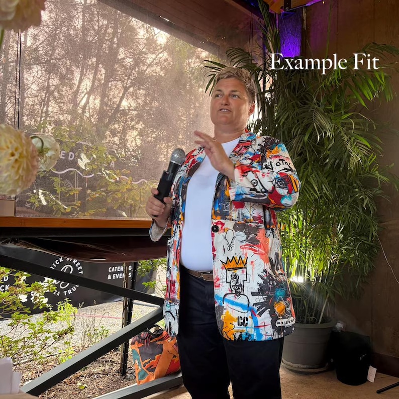 May include: A blazer featuring a vibrant, multi-colored graffiti-style print with black, red, blue, and yellow accents over a white base. The garment is worn over a plain white t-shirt and dark trousers. The text "Example Fit" appears in the corner.