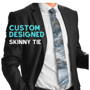 May include: A skinny tie featuring a detailed illustration of a dragon in a snowy, rocky landscape. The tie is worn with a white dress shirt and a black suit jacket. The text CUSTOM DESIGNED SKINNY TIE is printed in blue and white on the left side.