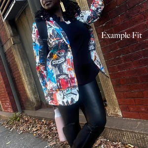 May include: A white blazer featuring a vibrant, multi-colored graffiti-style print with bold black, blue, and red abstract patterns. The blazer is worn over a solid black top and black leggings. The text "Example Fit" is visible on the right side.