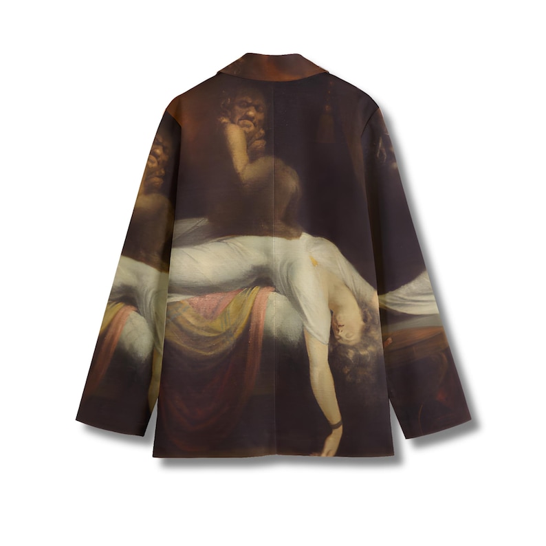 May include: A long-sleeve blazer featuring a dark, dramatic art print of a figure in a white garment reclining on a bed with a dark, shadowy creature looming above. The jacket has a structured collar, long sleeves, and a straight hemline.
