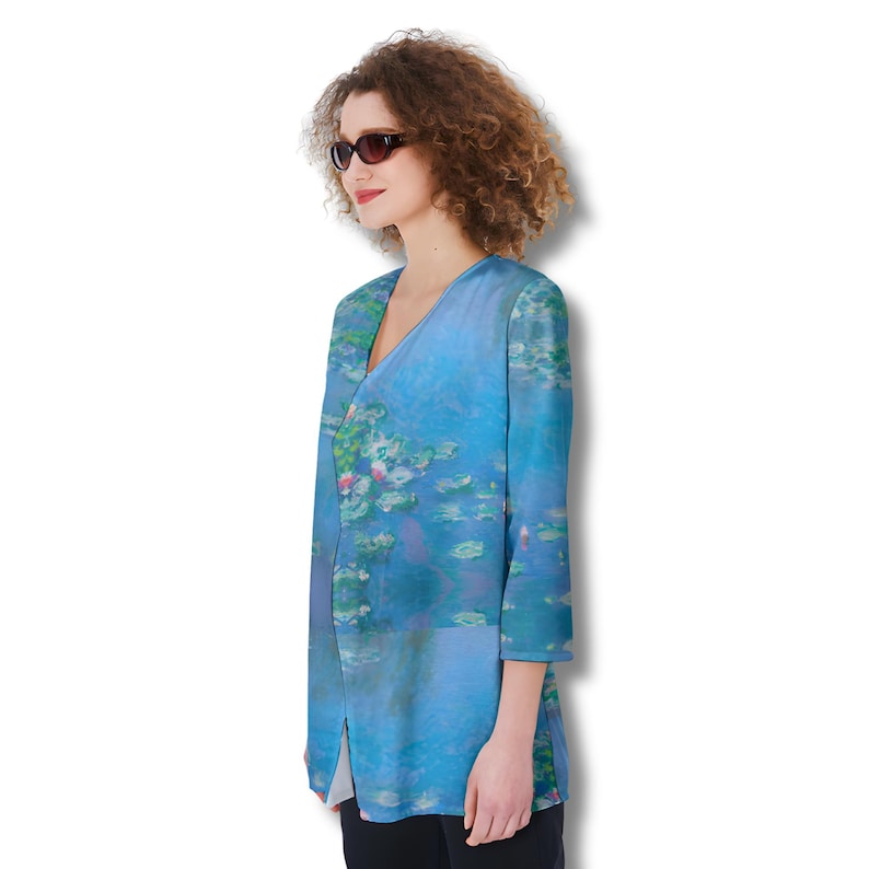 Puede incluir: Una blusa de manga larga con cuello en V con una pintura de nen&uacute;fares en tonos azules, verdes y rosas. La blusa tiene una abertura frontal y mangas tres cuartos. La obra de arte recuerda a las pinturas impresionistas.