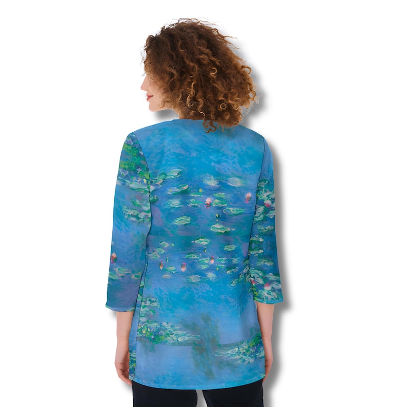 Puede incluir: Una t&uacute;nica azul con un dise&ntilde;o de pintura de nen&uacute;fares. La t&uacute;nica tiene mangas tres cuartos y cuello en V. La obra de arte presenta tonos de azul, verde y rosa, que representan nen&uacute;fares en un estanque. La prenda est&aacute; hecha de una tela suave y fluida.
