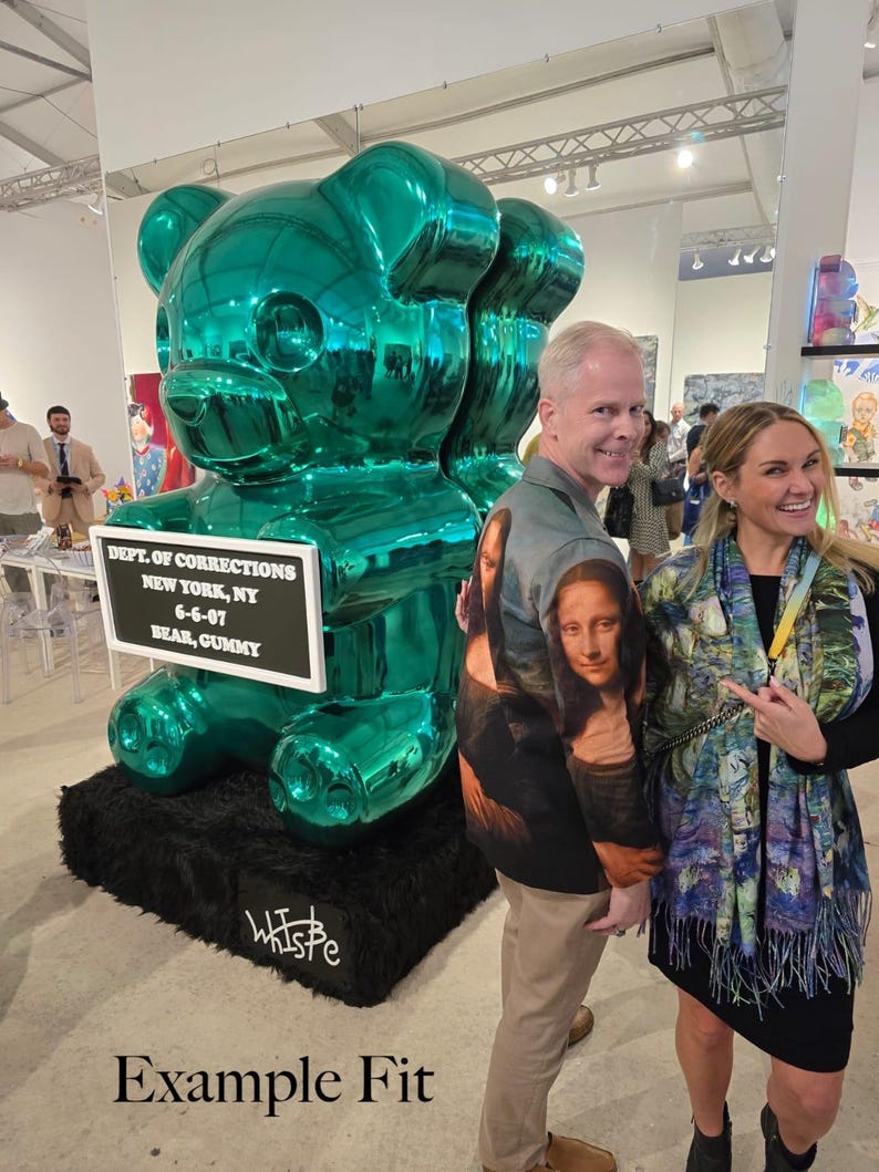 May include: A large, metallic emerald green sculpture of a gummy bear standing on a black base. A white rectangular sign attached to the bear reads: DEPT. OF CORRECTIONS, NEW YORK, NY, 6-6-07, BEAR, GUMMY. The artist signature is written in white on the base.
