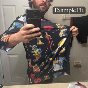 Puede incluir: Una camisa negra de manga larga con un estampado surrealista colorido. El dise&ntilde;o incluye varias figuras y objetos abstractos en tonos rojos, amarillos, azules y naranjas. El texto "Example Fit" es visible en la esquina superior derecha.
