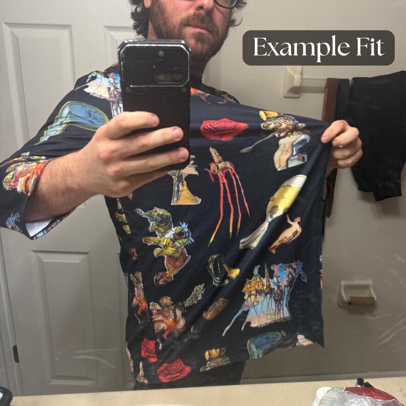 Puede incluir: Una camisa negra de manga larga con un estampado surrealista colorido. El dise&ntilde;o incluye varias figuras y objetos abstractos en tonos rojos, amarillos, azules y naranjas. El texto "Example Fit" es visible en la esquina superior derecha.
