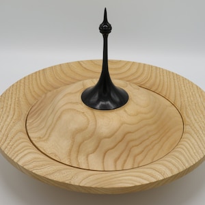 May include: A wooden bowl with a lid. The bowl is made of light wood with a natural grain pattern. The lid has a black wooden finial on top.