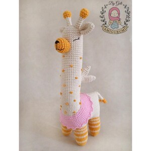 Può includere: Un giocattolo amigurumi a forma di giraffa realizzato a uncinetto con filato bianco e dettagli gialli e arancioni. La girafe indossa un tutù rosa e ha un'espressione amichevole.