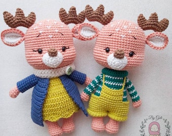 Op de afbeelding: Twee gehaakte herten knuffels, een met een blauw jasje en een gele jurk, de andere met een groen-wit gestreept shirt en een gele overall. Beide hebben een roze lichaam, bruine gewei en een wit gezicht.