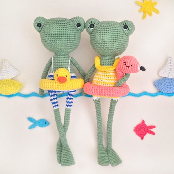 Puede incluir: Dos juguetes de rana de crochet que llevan trajes de baño y sostienen flotadores de piscina inflables. La rana de la izquierda lleva un traje de baño amarillo con un patrón de rayas azules y blancas y sostiene un flotador de pato amarillo. La rana de la derecha lleva un traje de baño de rayas rosas y amarillas y sostiene un flotador de flamenco rosa.