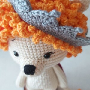 May include: A crocheted lion toy with a gray crown and orange mane. The lion is sitting on a wooden base.