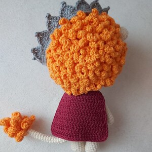 May include: A crocheted lion toy with a gray crown, orange mane, burgundy cape, and a white tail.