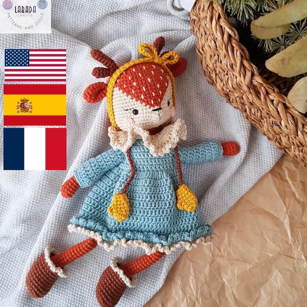 Puede incluir: Una muñeca de crochet de ciervo con un vestido azul con detalles amarillos y zapatos marrones. La muñeca está tumbada sobre una manta blanca con un fondo de papel marrón.