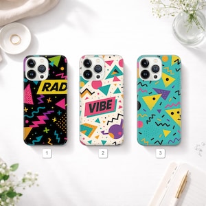 Op de afbeelding: Drie telefoonhoesjes met kleurrijke geometrische ontwerpen. De eerste hoes is zwart met het woord "RAD" en roze, gele en groene vormen. De tweede hoes is crèmekleurig met het woord "VIBE" en roze, turquoise en paarse vormen. De derde hoes is turquoise met gele en paarse vormen.