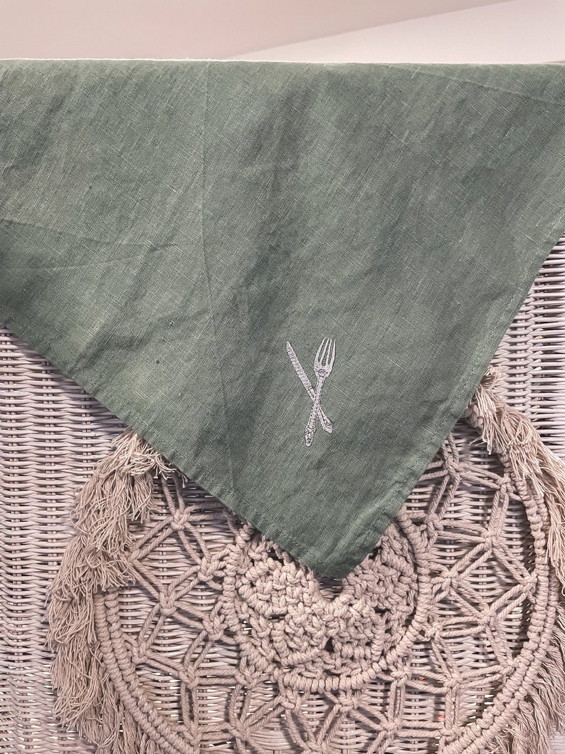 May include: A green linen kitchen towel with a white embroidered design of a fork and knife.