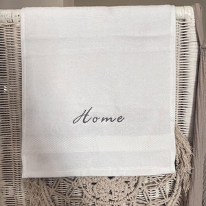May include: White hand towel with the word "Home" embroidered in black cursive lettering.