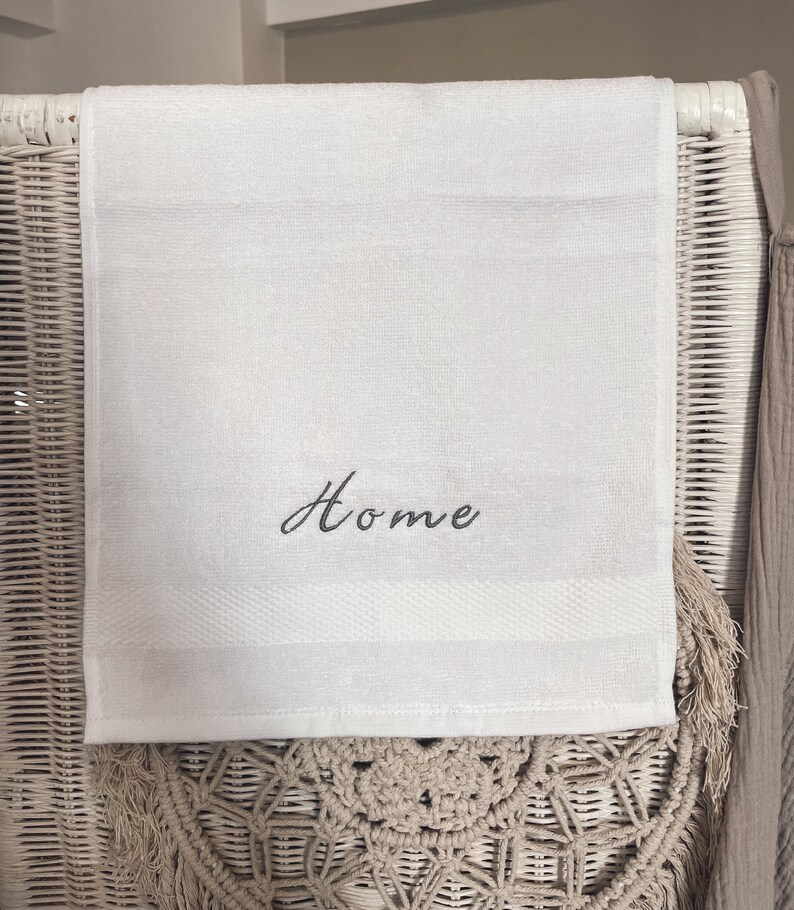 May include: White hand towel with the word "Home" embroidered in black cursive lettering.