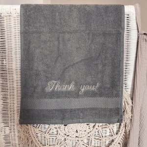 May include: A dark gray hand towel with the words "Thank you!" embroidered in white.