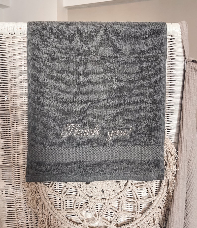 May include: A dark gray hand towel with the words "Thank you!" embroidered in white.