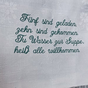 May include: Embroidered white linen kitchen towel with the text "F&uuml;nf sind geladen, zehn sind gekommen. Tu Wasser zur Suppe, hei&szlig; alle willkommen."