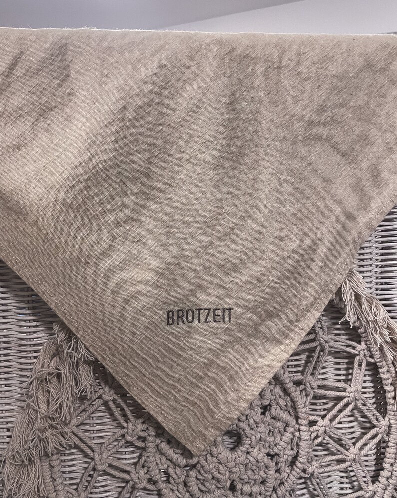 Puede incluir: Una bolsa de pan de lino beige con la palabra "BROTZEIT" impresa en negro.