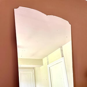 Peut inclure: Un miroir rectangulaire avec un bord supérieur festonné. Le miroir reflète une pièce avec des portes blanches et une table recouverte d'une nappe blanche. Le miroir a un aspect vieilli et décoloré.