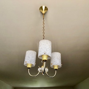 May include: A gold chandelier with three frosted glass shades hanging from a chain.