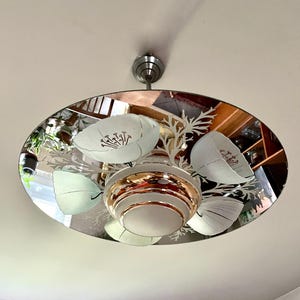 May include: A mirrored ceiling light fixture with a floral design. The fixture has a circular, mirrored base with a copper-colored center. The floral design features white flowers and leaves.