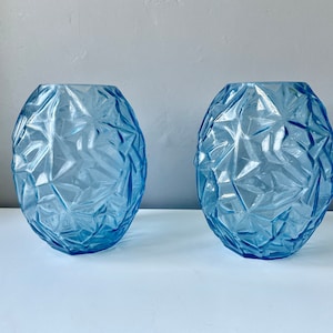 May include: Two blue glass vases with a geometric, faceted design. The vases are round and have a textured surface.