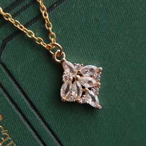 May include: A gold chain necklace with a delicate pendant featuring a cluster of clear cubic zirconia stones arranged in a flower shape.