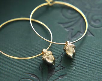 Puede incluir: Un par de pendientes de aro de oro con abalorios de bellota. Los pendientes son simples y elegantes, y los abalorios de bellota añaden un toque de fantasía.