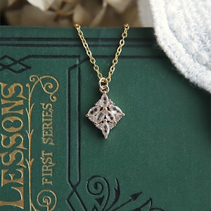 May include: A gold necklace with a delicate pendant featuring a cluster of clear cubic zirconia stones arranged in a flower shape.