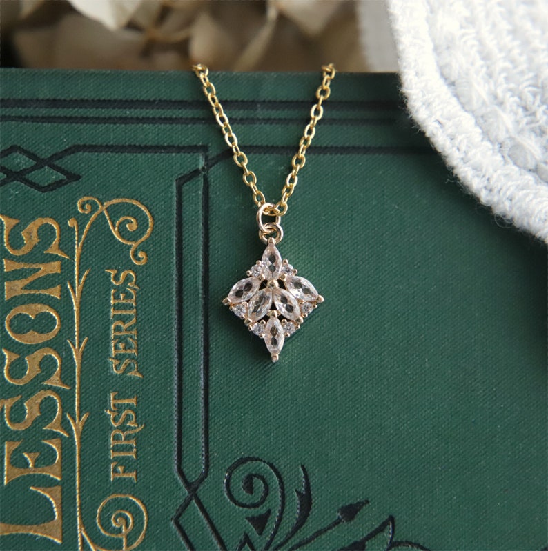May include: A gold necklace with a delicate pendant featuring a cluster of clear cubic zirconia stones arranged in a flower shape.