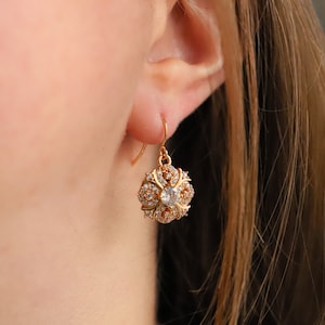May include: Gold dangle earrings with a flower-shaped design featuring clear cubic zirconia stones.